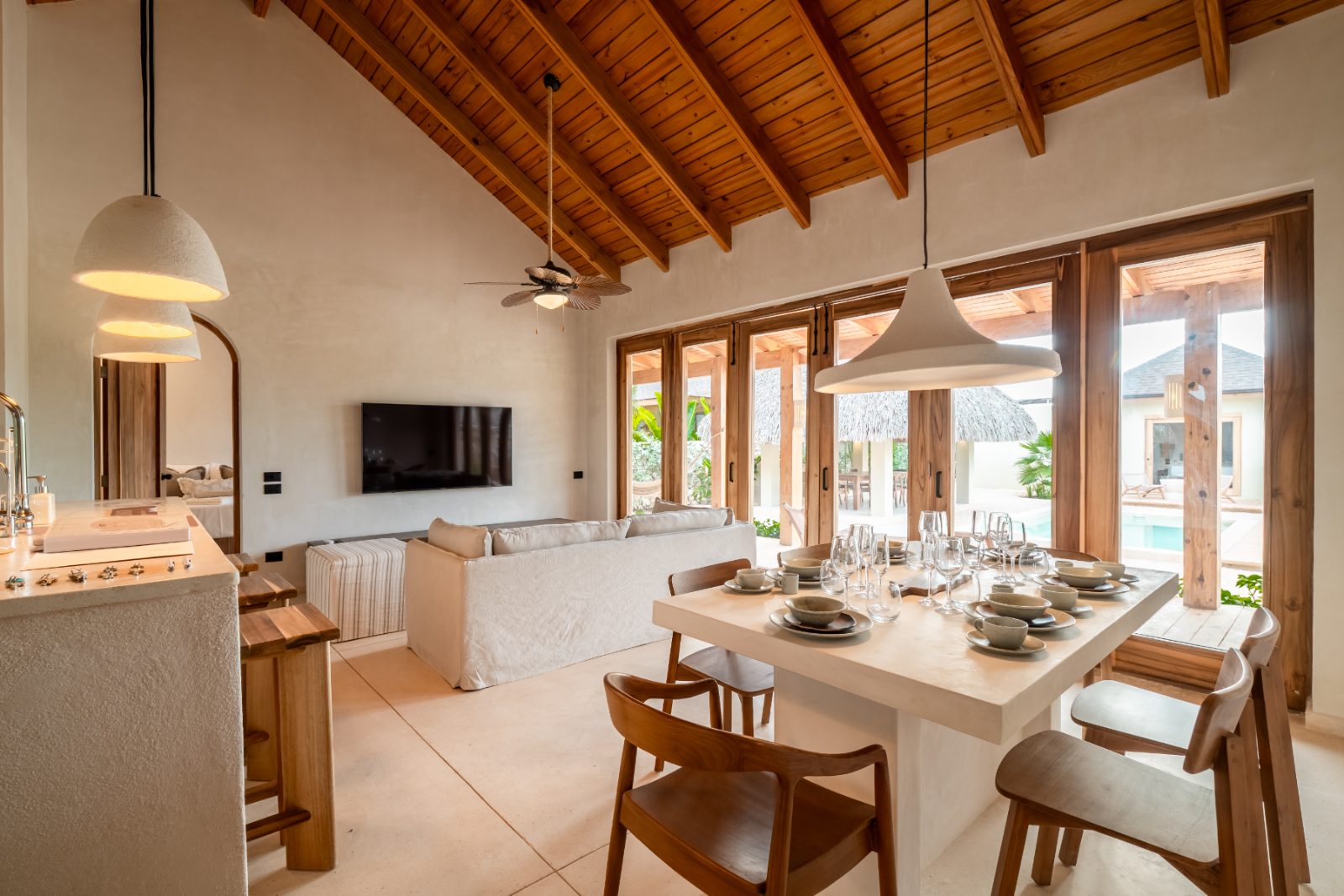Open living and dining space under a timber ceiling looking out to the pool