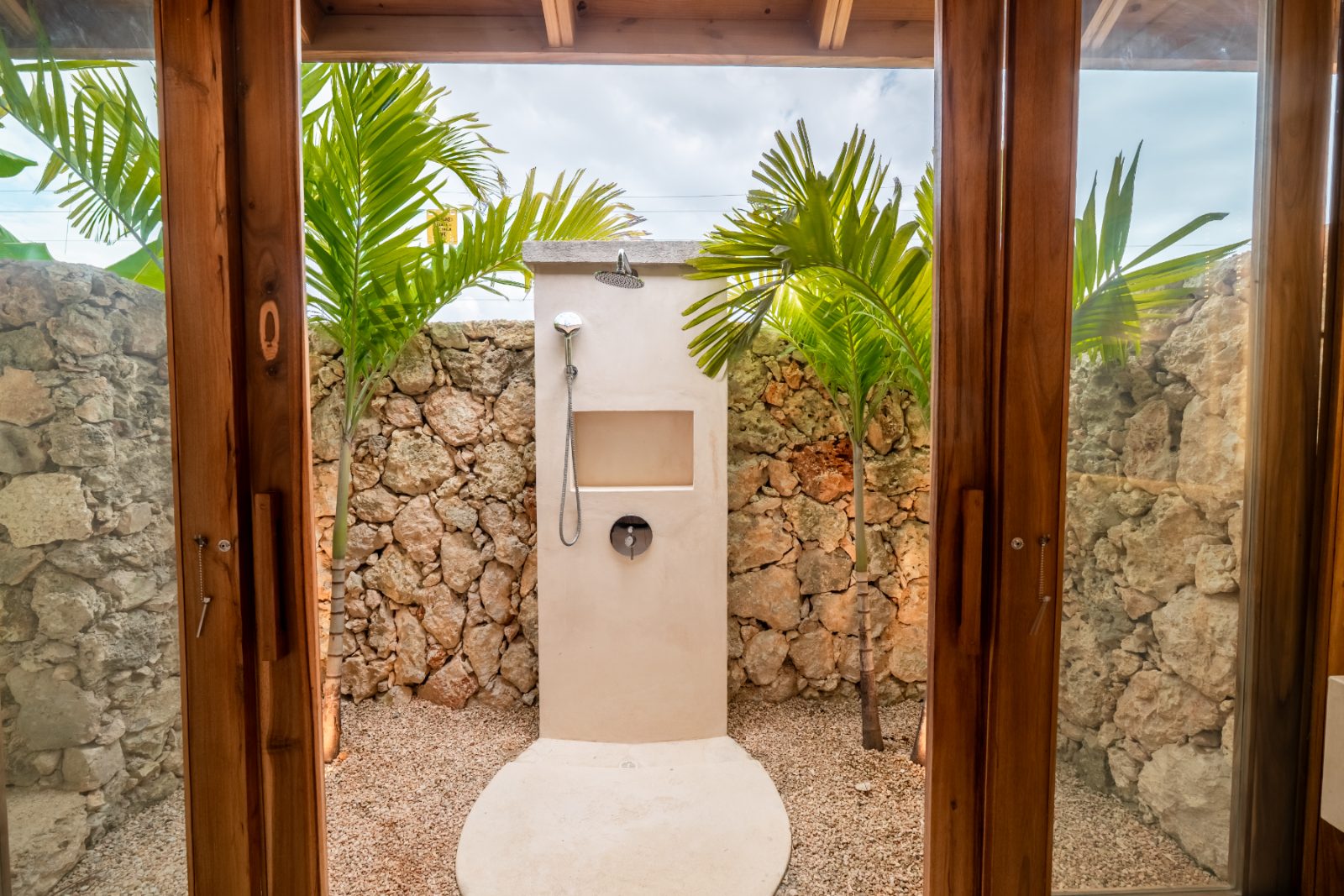 Outdoor shower against a coral stone wall framed by palms