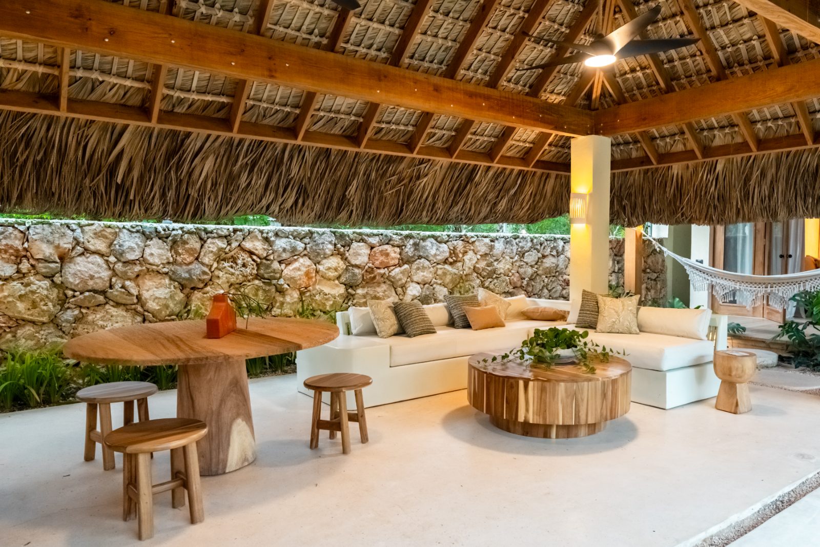Palapa lounge with built-in sofa, round timber tables and stone wall
