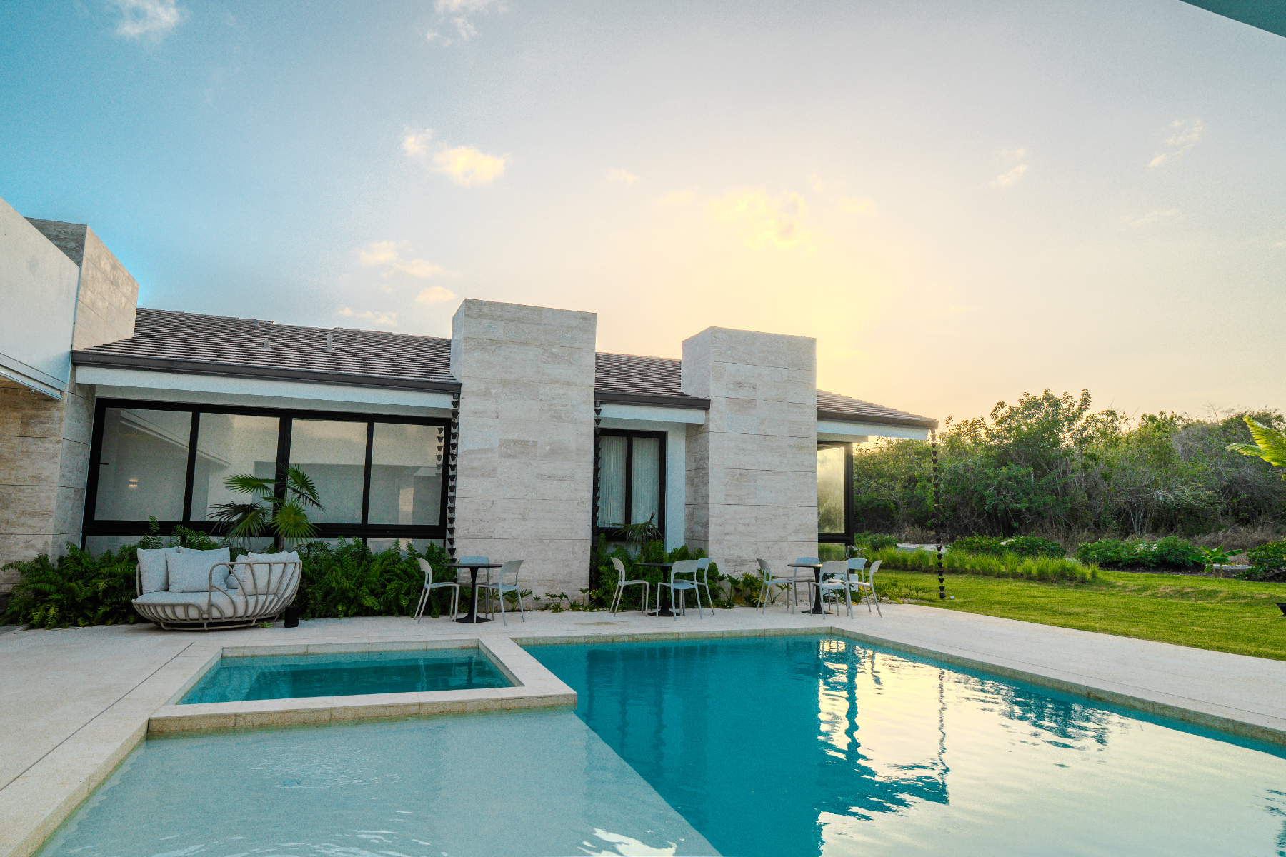 Pool and spa beside the travertine façade with lounge seating at dusk