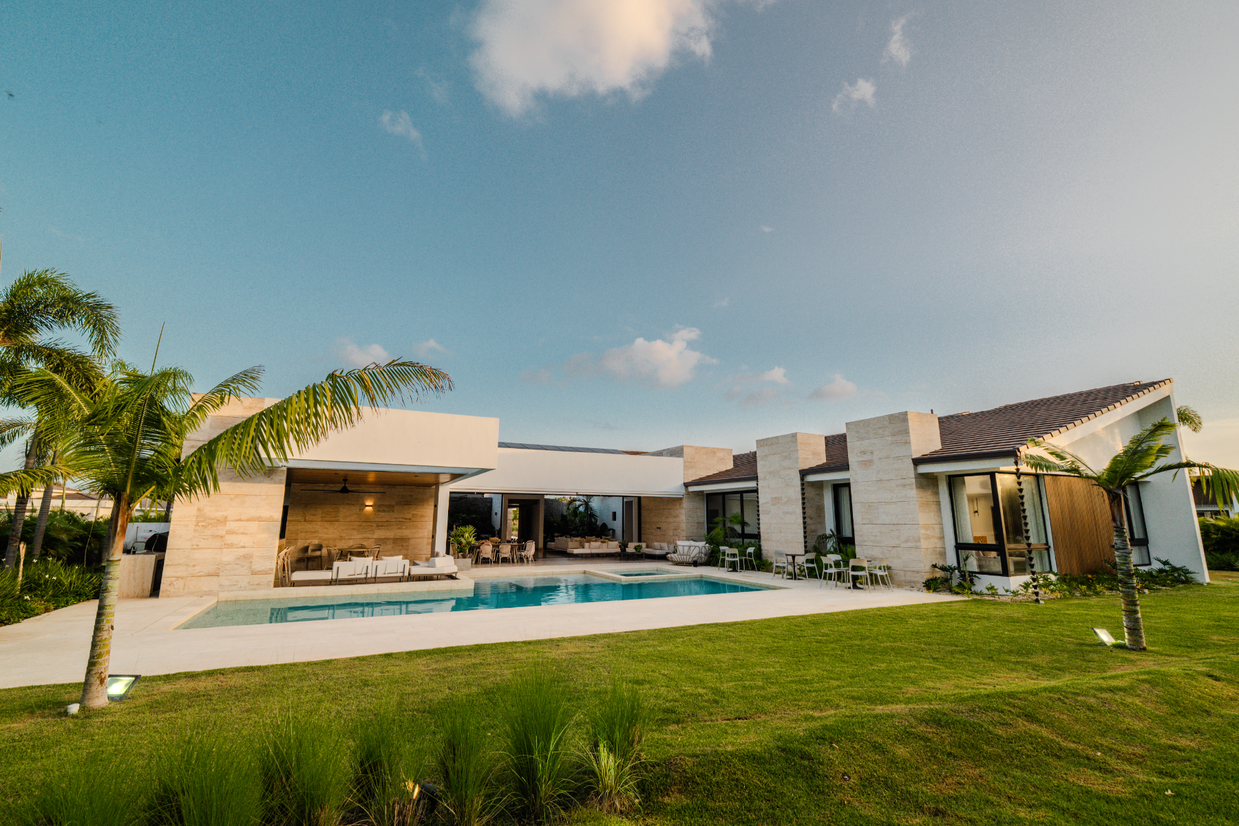 Villa seen across the lawn with pool, palms and open living pavilion